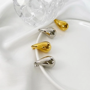Polished teardrop earrings in gold and silver finish displayed on a ceramic plate