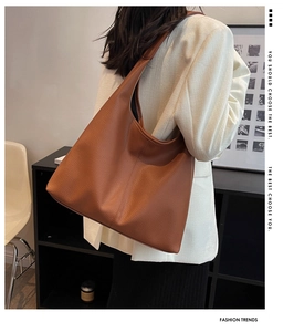 Close-up of brown pebbled leather hobo bag with wide shoulder strap on white suit