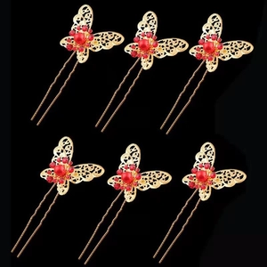 Detailed close-up of golden butterfly hair pins with red pearls and rhinestones