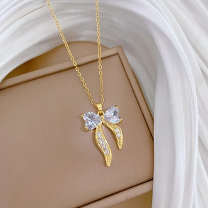 Elegant gold bow necklace with crystal heart accents on a soft beige jewelry gift box