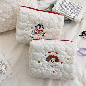 Close-up of white quilted cosmetic bags with cute dog embroidery and red zipper details