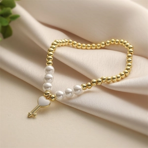 Bracelet élégant perles dorées et nacrées avec pendentif clé en cœur sur tissu soie