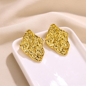 Macro shot of gold petal texture on diamond-shaped stainless steel earrings on a plate