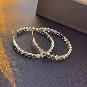 Detail of gold C-shaped hoop earrings with colorful round gemstones on leather surface