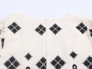 Detail of ethnic embroidery and invisible zipper on a cream cotton linen dress back