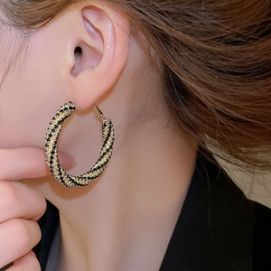 Close-up of black and gold braided large hoop earrings worn with elegant dark suit