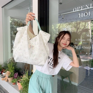 Close-up of white canvas tote bag with floral rabbit pattern and green woven handles