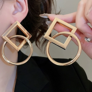 Close-up of interlocking square and circular gold geometric earrings on a model