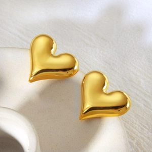 Macro view of gold heart stud earrings with polished finish on a ceramic surface