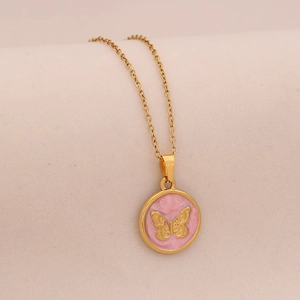 Macro detail of golden round pendant featuring a pink background with relief butterfly