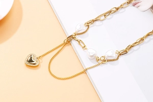 Détail du collier doré multicouche avec perles baroques blanches et pendentif cœur