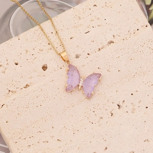 Gros plan du collier papillon doré avec ailes violettes sur un support en pierre