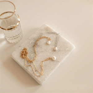 Detail view of baroque pearl necklaces on a white marble tray with gold-rimmed glass