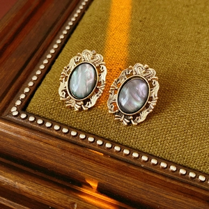Close-up of vintage golden earrings with oval dark iridescent resin inlay on green fabric