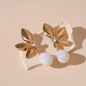 Close-up of golden leaf earrings with shimmering zircon and iridescent drop pearl charms