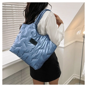 Blue quilted puffer tote bag with black fashion label shown on model shoulder