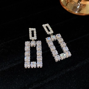 Macro shot of silver hollow rectangular earrings with inlaid sparkling crystals on black velvet