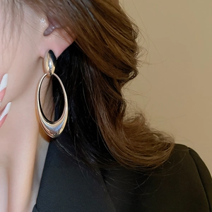 Close-up of model wearing silver oval hollow drop earrings with high-polish metallic finish