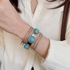Detail of multi-layer silver metal bracelet with turquoise stones on white sleeve