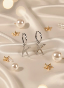 Detail of silver letter K pendant hoop earring resting on luxury cream silk fabric