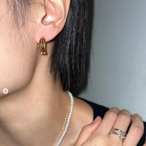 Detailed shot of gold twisted hoop earrings paired with a white pearl necklace on model