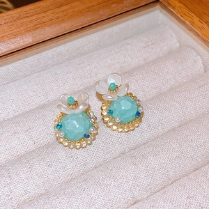 Macro detail of wheat ear tassel earrings with mint green gemstone in a wooden jewelry box