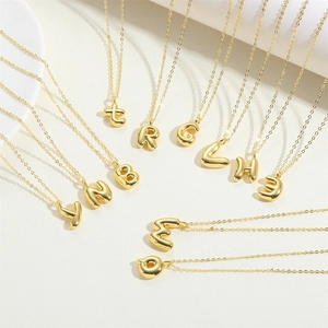 Multiple 3D bubble initial necklaces in 14K gold plating on a textured beige surface