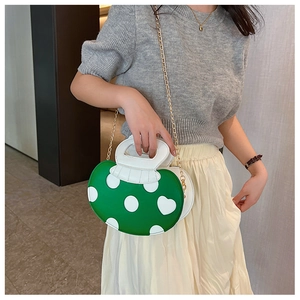 Detail of mushroom shaped green and white handbag with heart patterns and gold chain strap