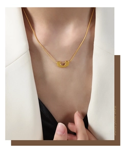 Détail d'un pendentif en U doré sur une chaîne serpent porté avec un blazer blanc élégant