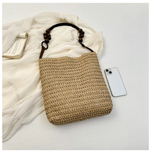 Detail view of beige straw woven bag with wooden bead handle on a white shirt