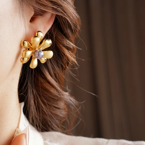 Detailed close-up of 18k gold flower earring with a purple pearl on the model's ear