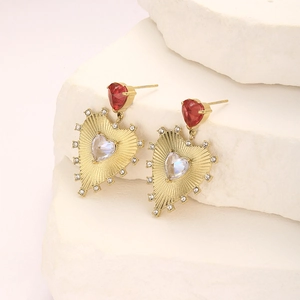 Detail of gold heart earrings with red zircon and iridescent stones on stone display