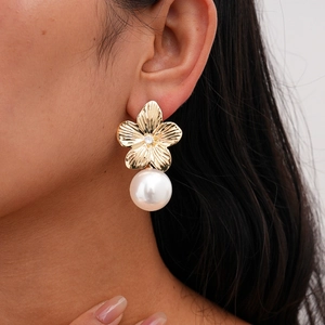 Close-up of golden flower earring with zircon center and large white pearl drop