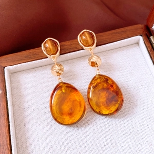 Detailed close-up of vintage amber resin water-drop earrings on a white fabric lining
