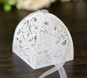 Close-up of white laser-cut wedding favor box with floral pattern and ribbon