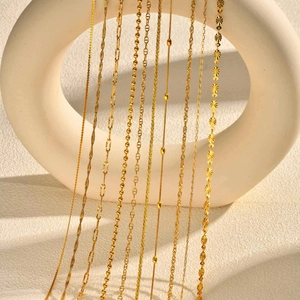 Collection of golden minimalist layered necklaces with various chain styles on white stand