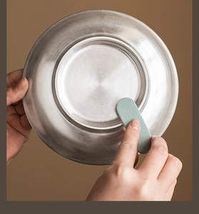 Close-up of green abrasive cleaning stick removing rust from a stainless steel bowl