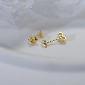 Detail view of gold clover stud earrings with white zircon on pleated fabric