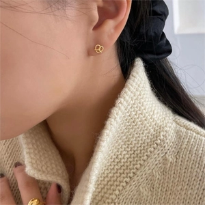 Close-up of a gold-tone twisted heart earring worn by a model in a beige knit sweater
