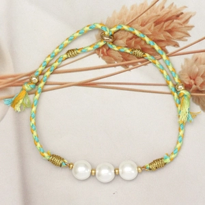 Detail of woven bracelet with glass pearls, gold beads and fringe on beige linen cloth