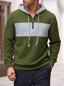 Detail of olive green waffle knit hoodie featuring grey patchwork and orange drawstring tips
