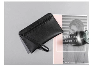 Detail of black pebbled leather clutch bag with metal zipper and wrist strap on grey background