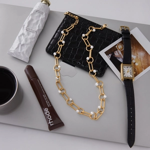 Flat lay of gold chain pearl necklace with vintage watch and croc-embossed pouch