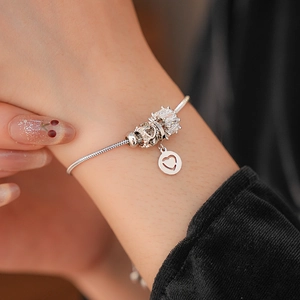 Macro shot of silver charm bracelet featuring heart pendant and crown bead on snake chain