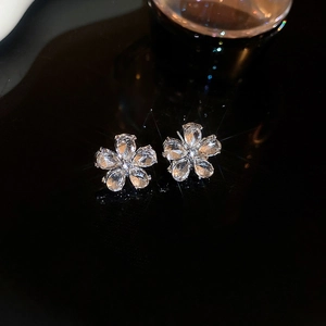 Close-up of sparkling floral stud earrings with clear crystals on a black reflective surface