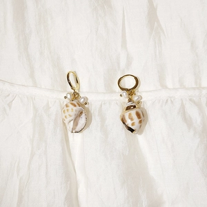 Macro detail of golden conch shell earrings with white pearls on white silk background