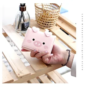 Close-up of pink pig-shaped tri-fold wallet with 3D heart ears held by a hand