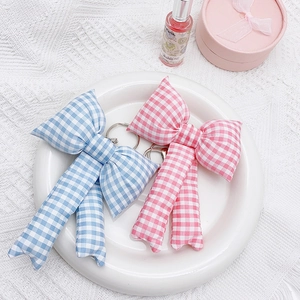 Pink and blue checkered fabric bow keychains displayed in a white ceramic dish