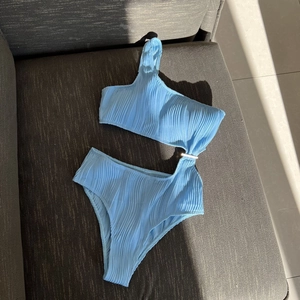 Detail of light blue textured fabric with cutout design and one-shoulder metallic buckle