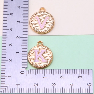Detailed view of pink enamel letter charms with gold border and ruler for size scale